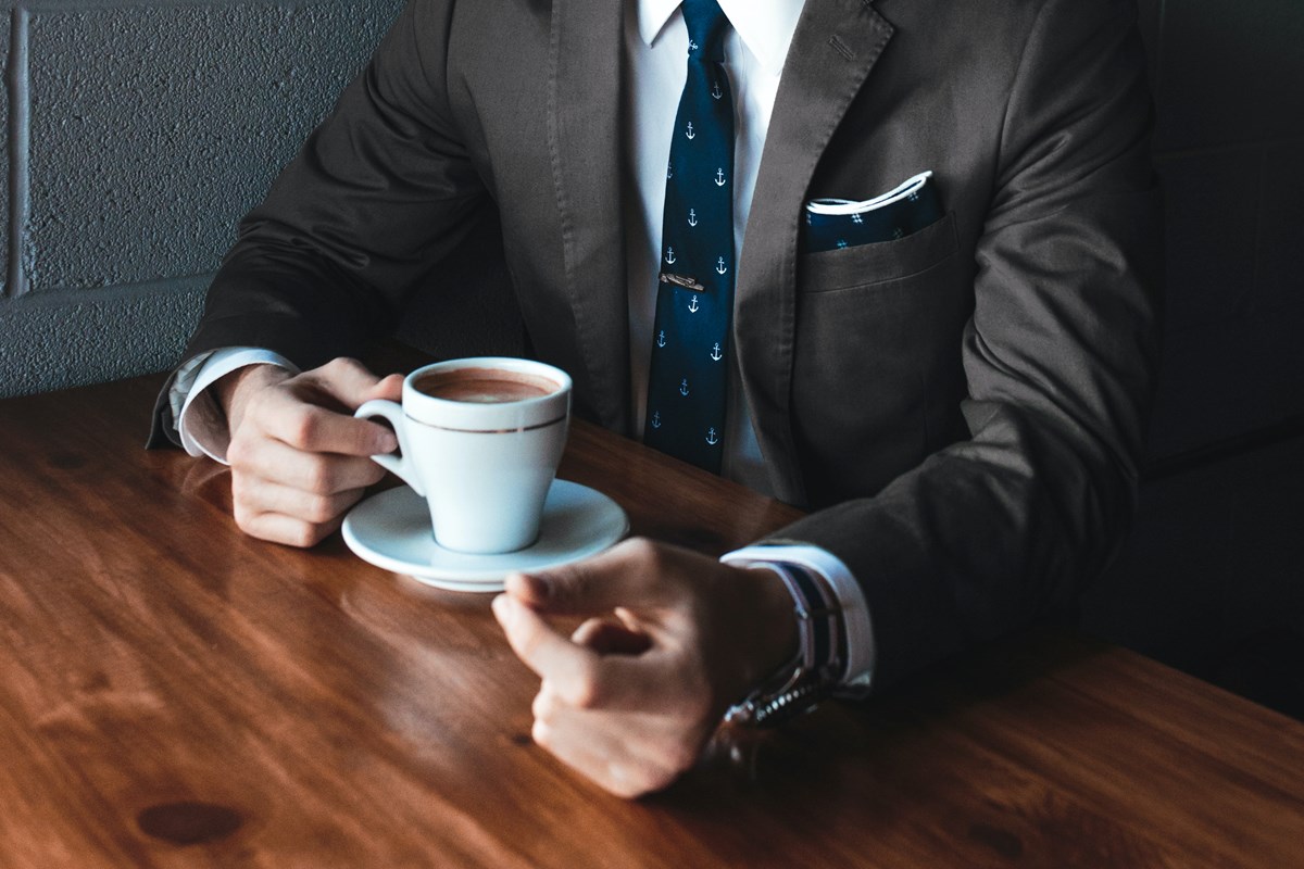 En bild på en man i kostym som håller i en kaffekopp.