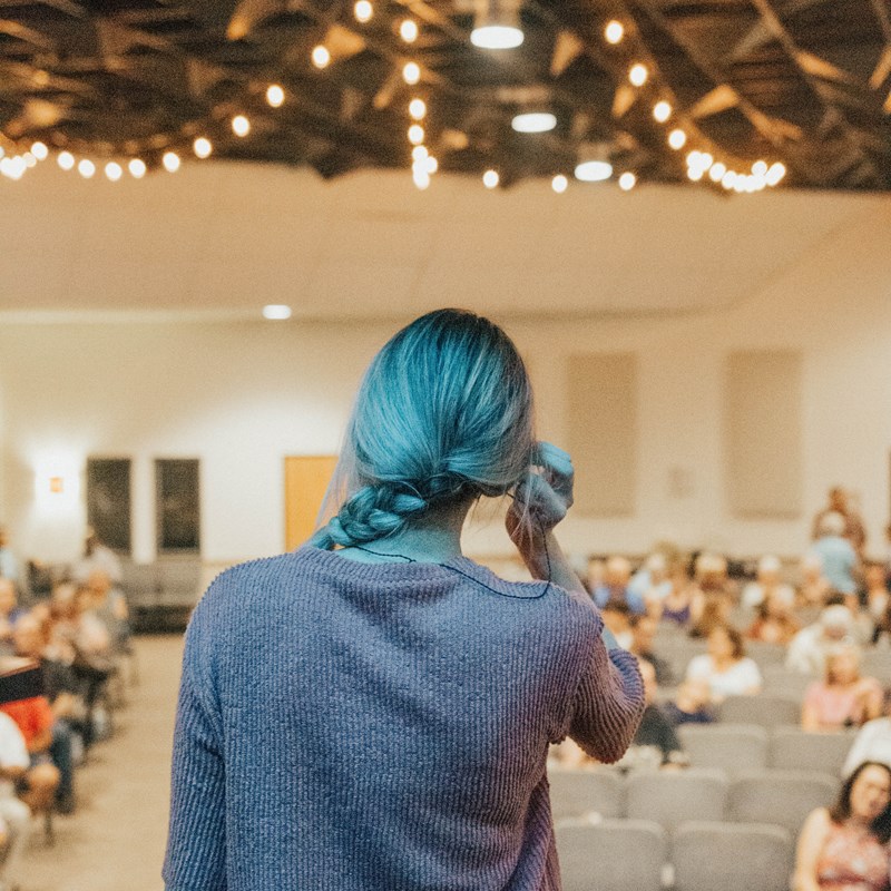 En bild på en kvinna som står på en scen för att hålla en föreläsning för en publik